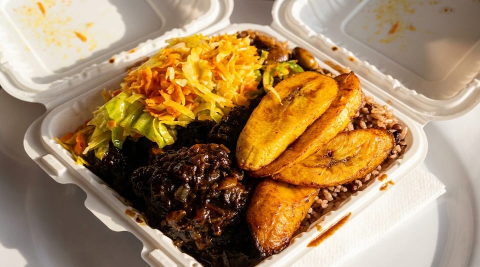 A takeout container filled with Jamaican oxtail, rice and peas, fried plantains, and steamed cabbage.
