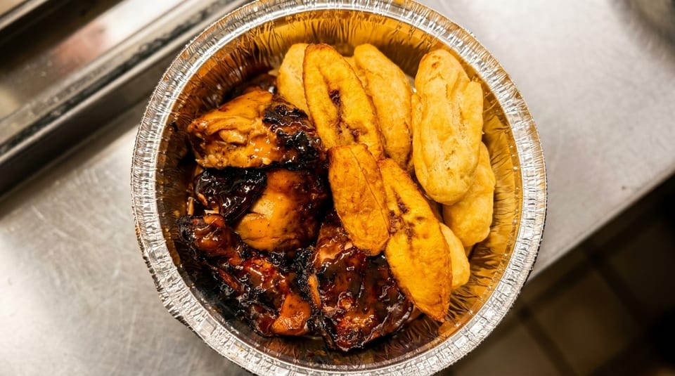 Takeout container filled with jerk chicken, fried plantains, and golden fried dumplings.